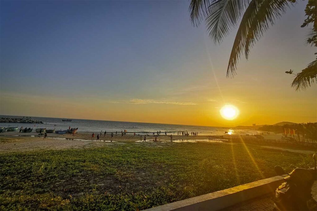 Sunset at Ong Dia Beach in Mui Ne with locals playing on the shore, basket boats lined up near the breakwater, and a warm golden sky reflected across the beach and sea.