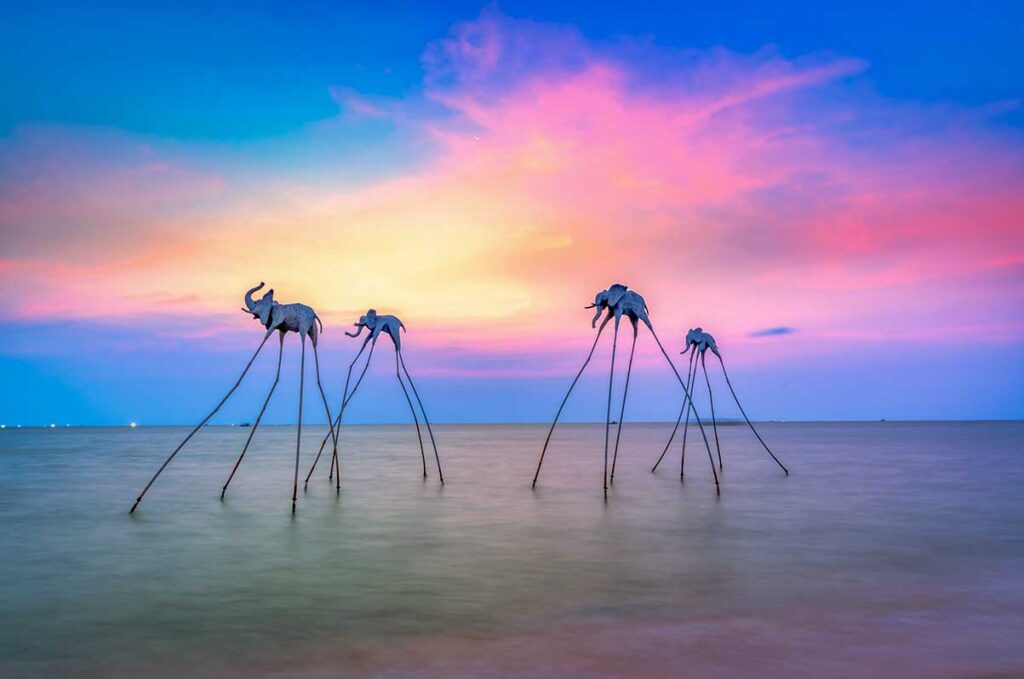 Colorful sunset over the west coast of Phu Quoc with artistic sea sculptures standing in calm ocean water