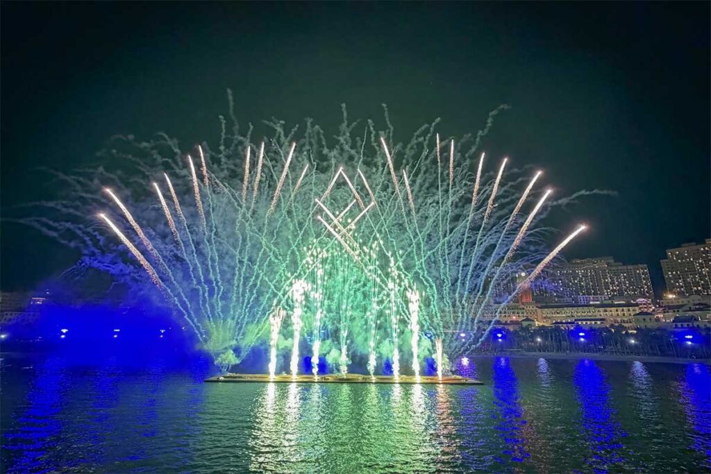Symphony of the Sea Phu Quoc fireworks show with green and white bursts rising from the water stage creating bright reflections on the sea in Sunset Town