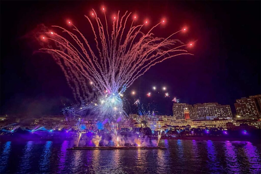 Symphony of the Sea Phu Quoc fireworks lighting up the night sky above Sunset Town with colorful explosions over the sea and illuminated waterfront buildings reflecting on the water