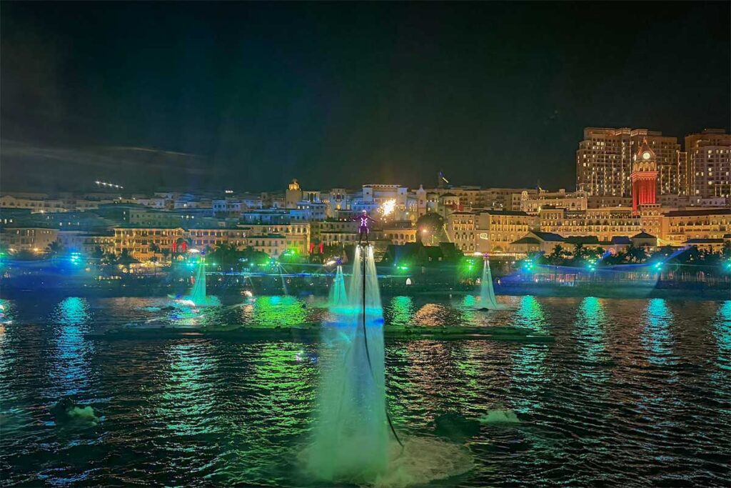 Symphony of the Sea Phu Quoc night performance with multiple flyboard riders illuminated in green light hovering above the water with Sunset Town skyline behind