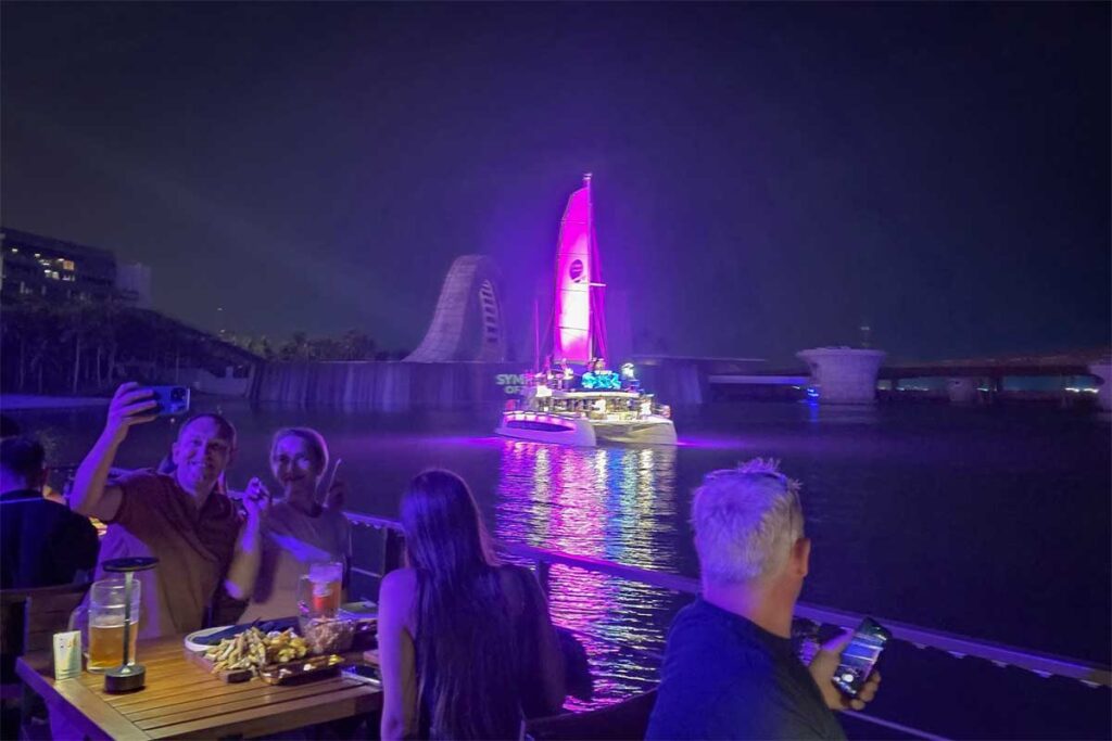 Visitors watching Symphony of the Sea Phu Quoc from a waterfront restaurant terrace with drinks and food while the show takes place on the sea at night