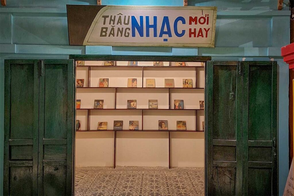 Replica 1950s Vietnamese music tape shop inside Lang Chai Xua Fish Sauce Museum, with original vinyl record covers displayed on wooden shelves behind old green doors