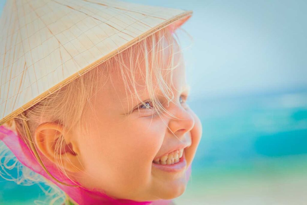 Smiling toddler wearing a Vietnamese hat on the beach in Phu Quoc during a family holiday