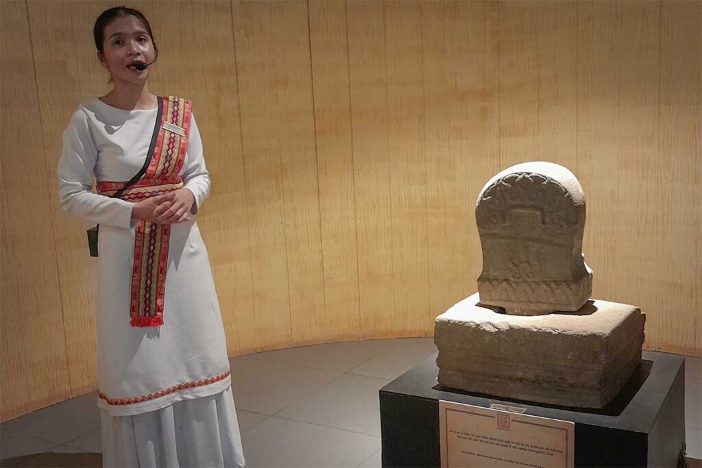 Tour guide in traditional dress explaining the Kut stone statue from the 15th century Champa Kingdom inside Lang Chai Xua Fish Sauce Museum
