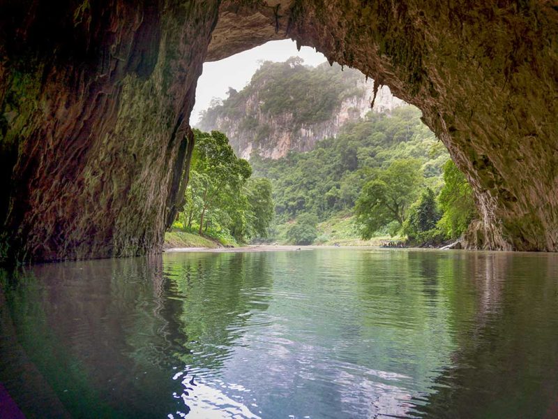Boat entering the Puong Cave entrance on Ba Be Lake, surrounded by limestone cliffs and lush forest during a Ba Be Lake tour in northern Vietnam.