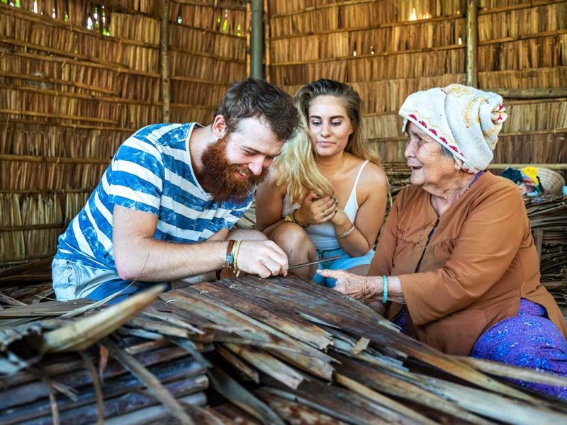 A local woman is showing traditional crafts to two tourist in a handicraft village in Cai Be