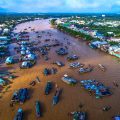 Cai Rang Floating Market Aerial View: Aerial view of the bustling Cai Rang floating market on the Mekong River, with Can Tho city's skyline visible in the distance.