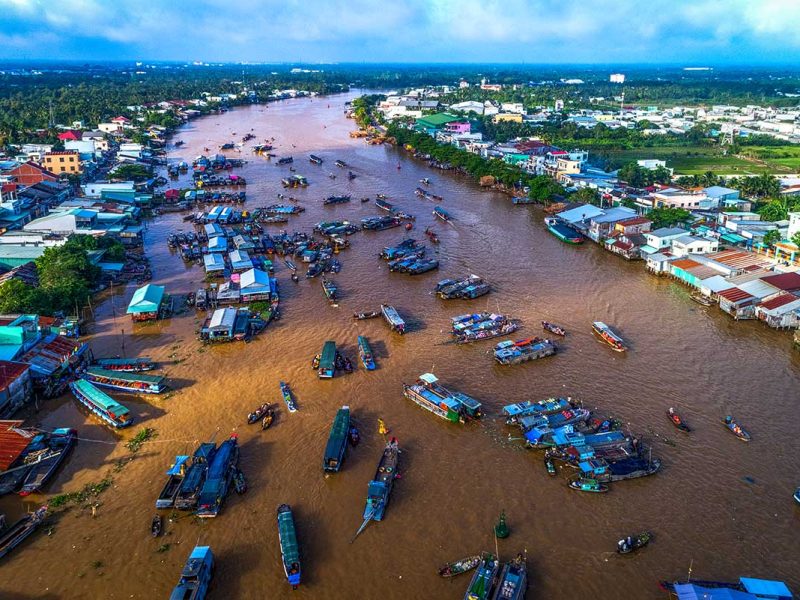 Cai Rang Floating Market Aerial View: Aerial view of the bustling Cai Rang floating market on the Mekong River, with Can Tho city's skyline visible in the distance.