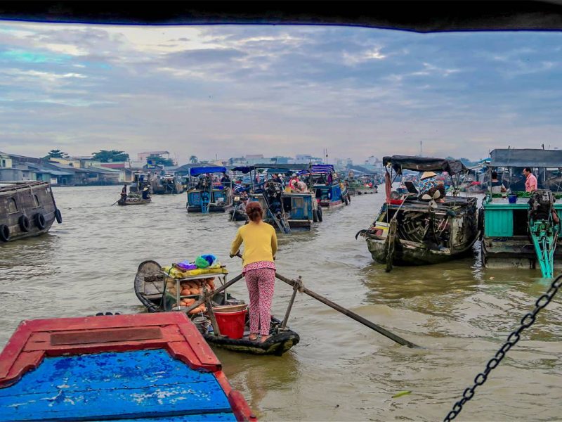 Early morning activity at Cai Rang Floating Market with small sampan serving food and drinks between rows of larger trading boats.