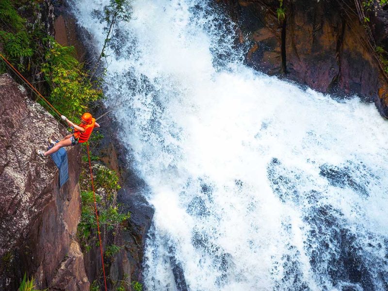 A man abseiling down a cliff next to a waterfall as part of canyoning in Dalat.