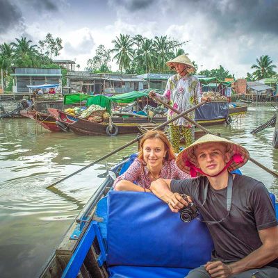 A tourist couple sitting in a traditional rowing boat while going through the canals of the Mekong Delta