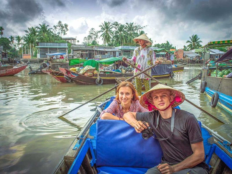 A tourist couple sitting in a traditional rowing boat while going through the canals of the Mekong Delta