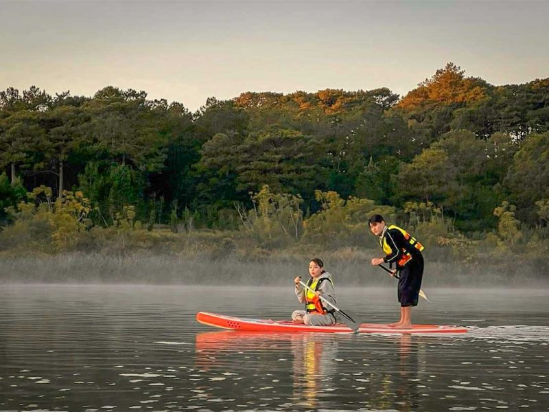 Couple stand-up paddling on Tuyen Lam Lake during a Dalat trekking and kayaking experience