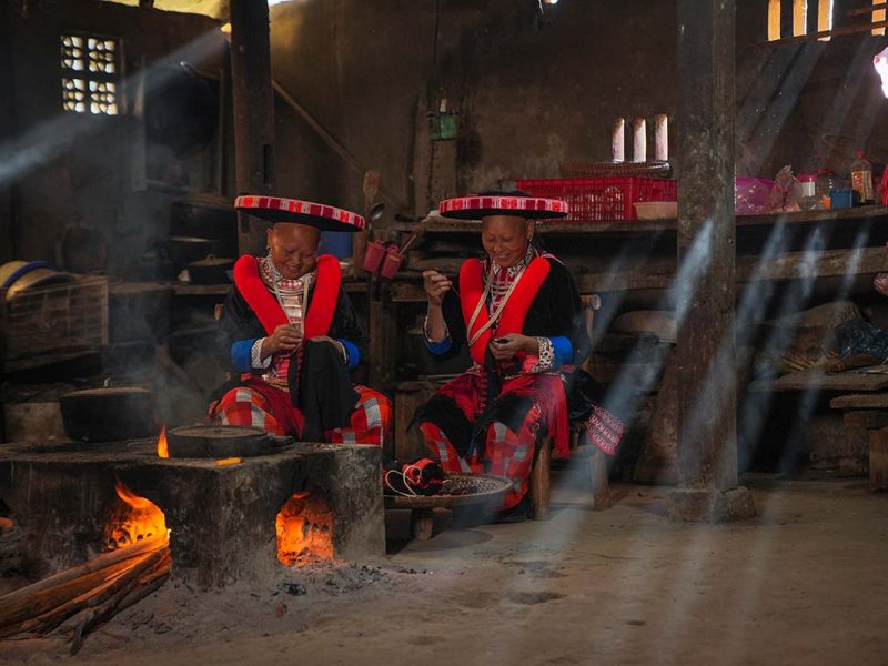Two Red Dao ethnic minority woman inside a house cooking on an open fire in Cao Bang