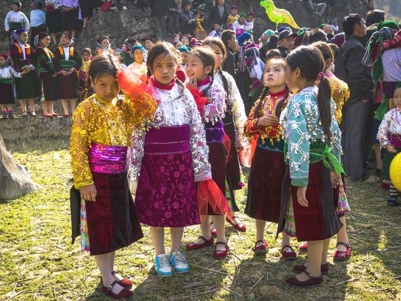 A group of ethnic children dressed in vibrant, shining traditional clothes, celebrating a festival in Ha Giang.