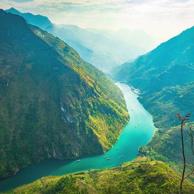 Ha Giang Loop in August – A spectacular view of the Nho Que River from Ma Pi Leng Pass, with lush green mountains and sunlight breaking through the clouds, highlighting the natural beauty of Ha Giang Loop in August.