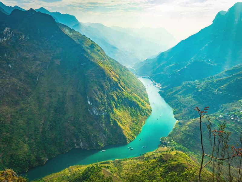 Ha Giang Loop in August – A spectacular view of the Nho Que River from Ma Pi Leng Pass, with lush green mountains and sunlight breaking through the clouds, highlighting the natural beauty of Ha Giang Loop in August.