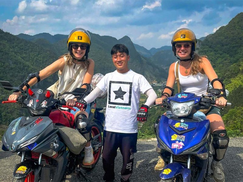Local Vietnam Easy Rider guide with guests on a Ha Giang Loop motorbike tour, stopping at a mountain viewpoint and showing real interaction between guides and travelers