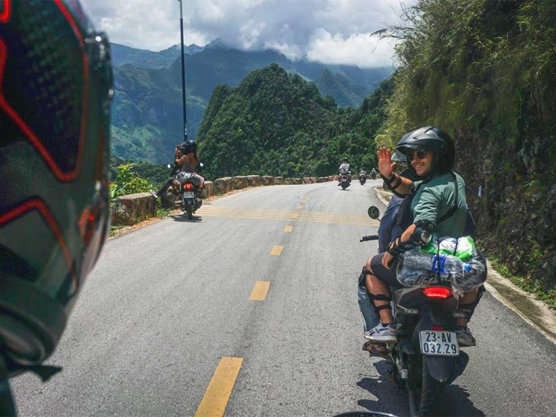 Ha Giang Loop motorbike tour with traveler on the back of an Easy Rider riding along a scenic mountain road