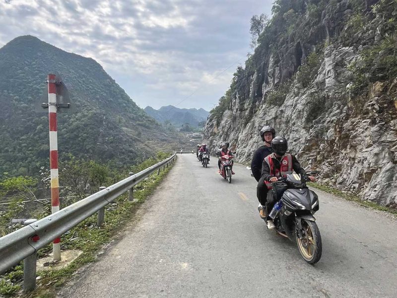 Group of tourists and Easy Riders riding motorbikes on a scenic Ha Giang Loop route