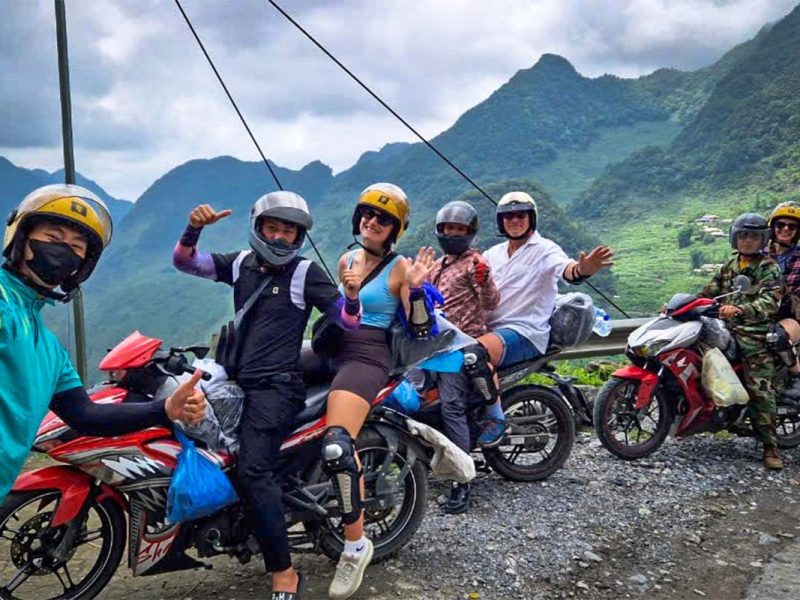 Ha Giang Loop group tour by Easy Rider motorbike with Local Vietnam, showing guests riding on the back of motorbikes with local drivers along a mountain road
