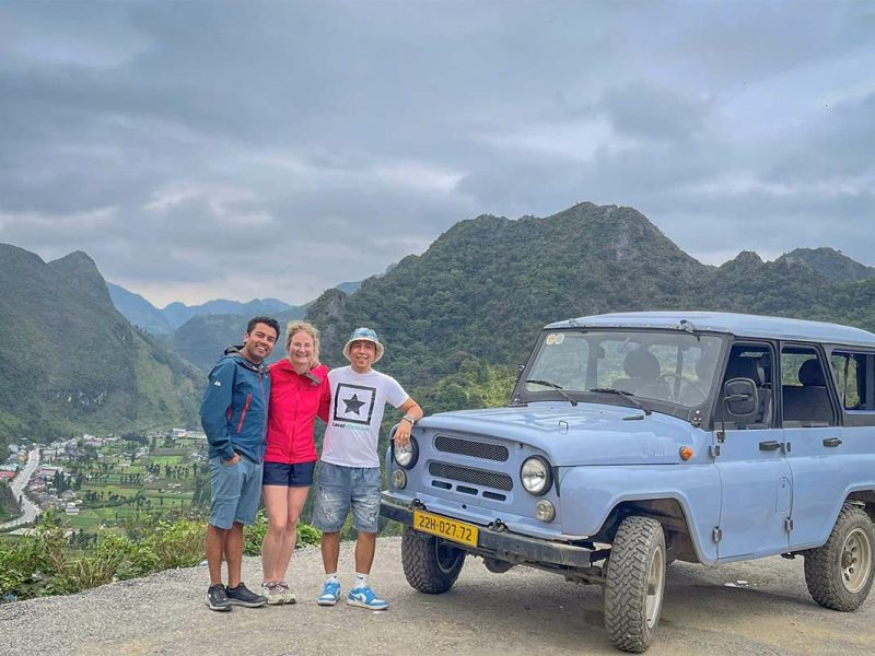 Local Vietnam guests and guide standing next to a classic jeep at a Ha Giang Loop viewpoint, photographed during an actual private tour and reflecting locally operated, experience-based travel.