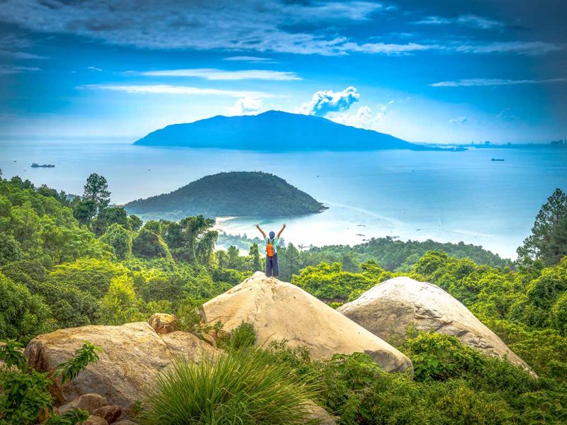 A tourist standing in the distance on a huge rock, overlooking the Hai Van Pass viewpoint with stunning coastal views - Vietnam nature