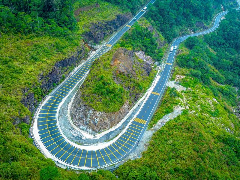 Aerial view of a dramatic hairpin bend on Khanh Le Pass, surrounded by dense forest and steep mountain slopes