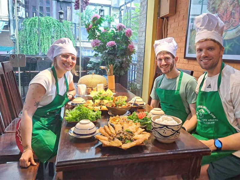 Small group seated with aprons and completed Vietnamese dishes during a Hanoi cooking class