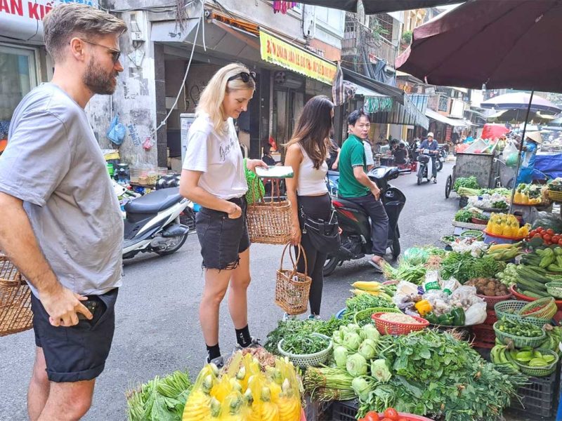 hanoi cooking class 9 Tourists with local guide examining fresh vegetables at a Hanoi market before their cooking class