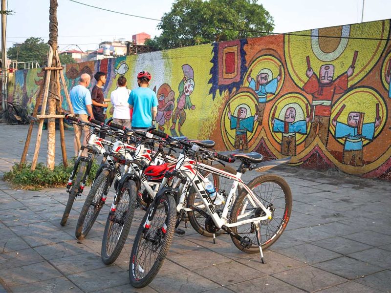 hanoi cycling tour 2 Bicycles parked near tourists and guide viewing the Hanoi mosaic wall on a cycling tour
