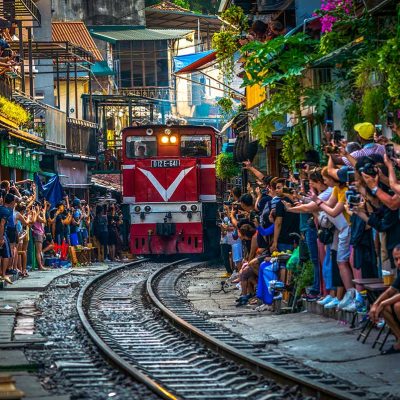 Hanoi Train Street with lots of tourists making photos of the incoming train through a narrow street with train track