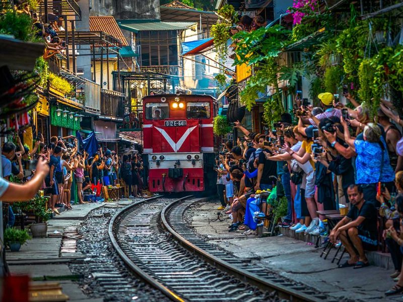 Hanoi Train Street with lots of tourists making photos of the incoming train through a narrow street with train track