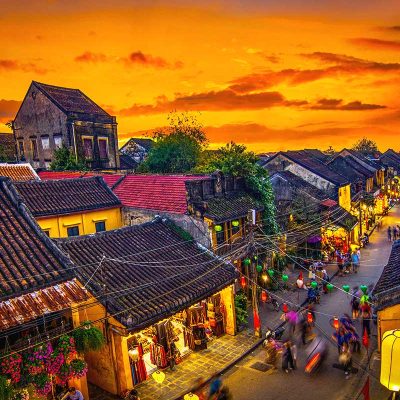 A view of the ancient town of Hoi An at sunset, creating a golden hue sky above the tiled roofs of the old houses.