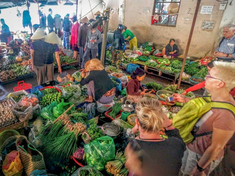 Tour participants shopping for fresh vegetables with a local guide at a traditional market in Hoi An.