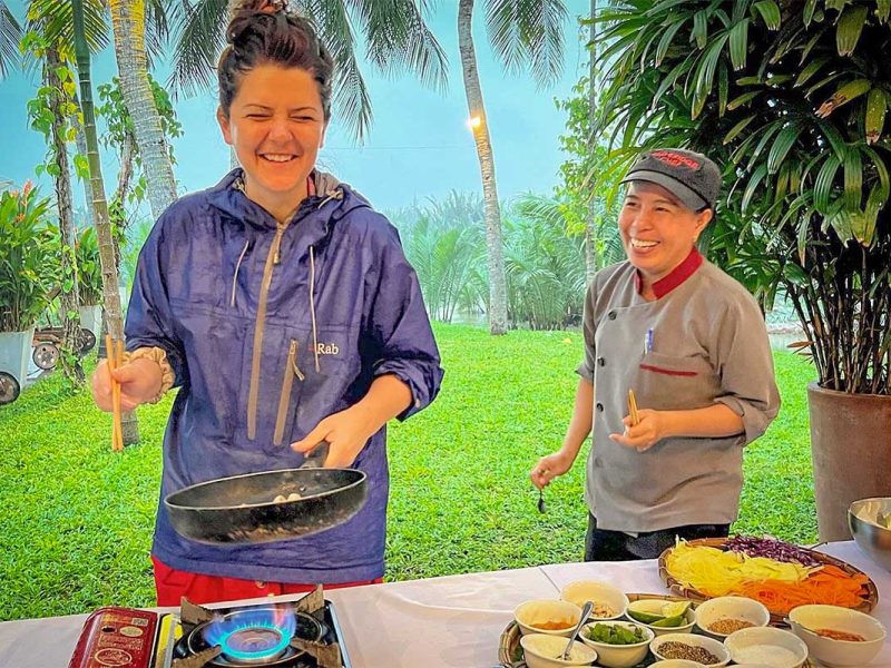Traveler smiling while cooking traditional Vietnamese dishes under the guidance of a local chef in Hoi An.