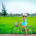 A traveller with conical hat on a bicycle is looking at the green rice fields during a countryside cycling ride around Hoi An