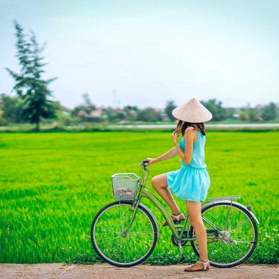 A traveller with conical hat on a bicycle is looking at the green rice fields during a countryside cycling ride around Hoi An