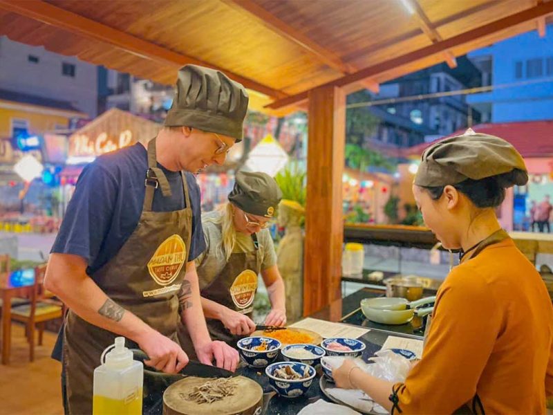 Hands-on Hue cooking class in Vietnam, with travelers chopping ingredients and preparing traditional dishes alongside a local chef.