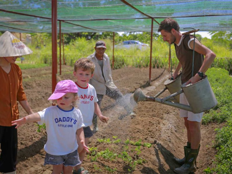 Family-friendly farming experience in Hue countryside, with visitors watering crops alongside local farmers.