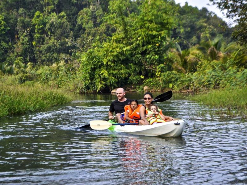 A man, woman, and child paddling a kayak along a peaceful stream, exploring the waterways of Cat Tien National Park.