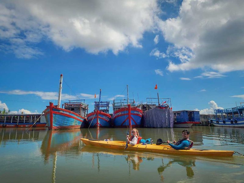 Kayaking past traditional fishing boats on the Thu Bon River during the Hoi An Old Town & Mangrove Tour