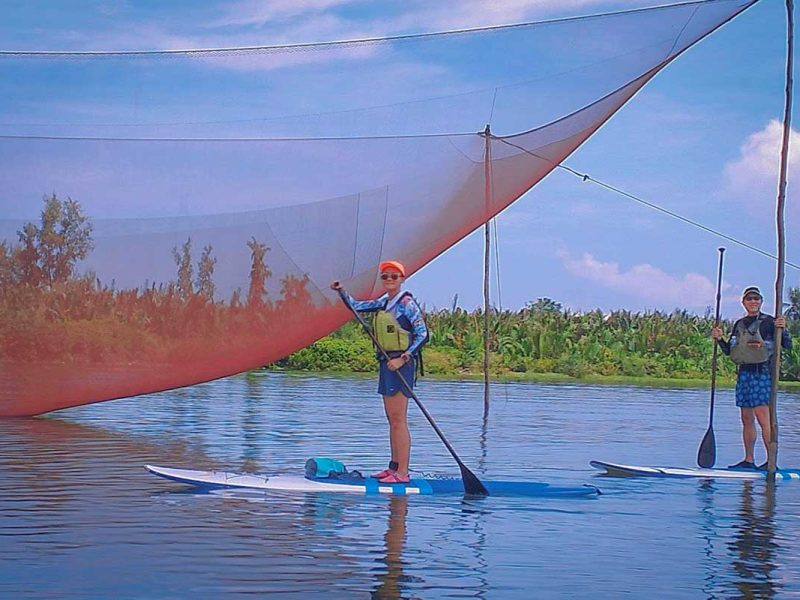 SUP travelers paddling near a giant Vietnamese fishing net along the waterways of Hoi An