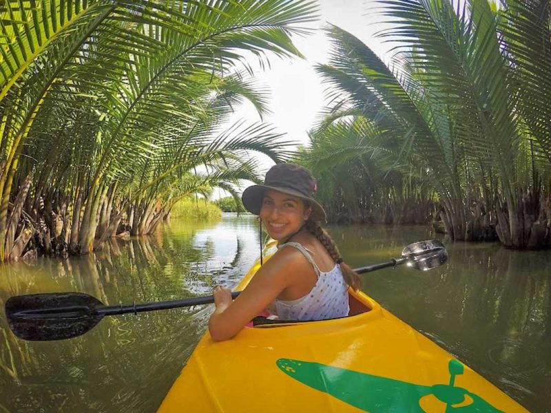 Smiling traveler kayaking through a tunnel of nipa palms in the Hoi An mangrove forest