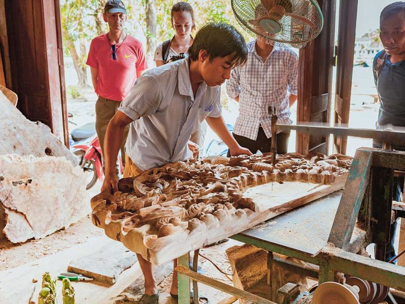 Local craftsman demonstrating intricate wood carving to visitors in Kim Bong Carpentry Village.