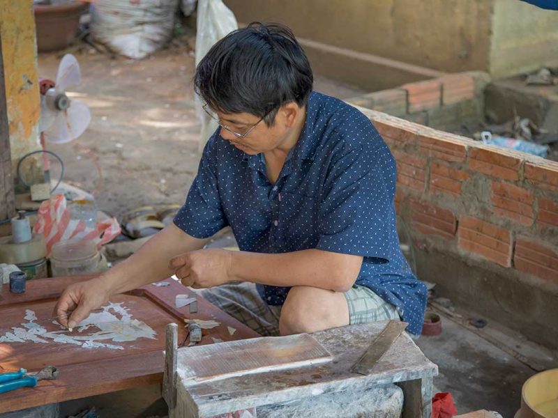 Artisan carefully inlaying mother-of-pearl into wood at Kim Bong Carpentry Village.