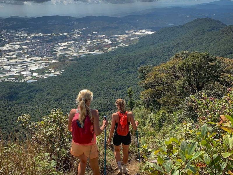 Hikers descending a scenic trail on a Langbiang Mountain trekking tour from Dalat, overlooking forested hills and farmland in the Central Highlands of Vietnam.