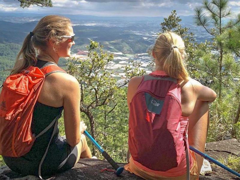 Hikers taking a break at a scenic viewpoint on a Langbiang Mountain trekking tour, overlooking valleys and farmland near Dalat, Vietnam.