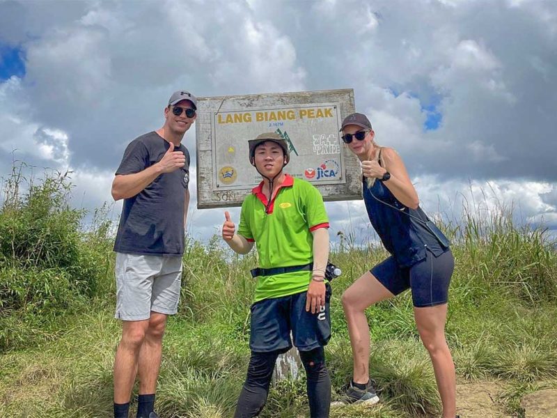 Group reaching Langbiang Peak during a guided Langbiang Mountain trekking tour, posing at the summit sign near Dalat.